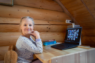 Wall Mural - Cute adorable caucasian little blond girl sitting at desk with laptop during online video chat school lesson session with teacher and class. Remote education concept. Self-isolation at quarantine