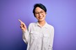 Young beautiful asian girl wearing casual shirt and glasses standing over purple background pointing finger up with successful idea. Exited and happy. Number one.