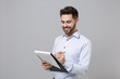 © ViDi Studio - Smiling young unshaven business man in light shirt posing isolated on grey background. Achievement career wealth business concept. Mock up copy space. Hold clipboard with papers document write notes.