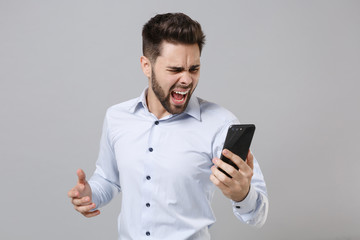 Canvas Print - Irritated angry young unshaven business man in light shirt isolated on grey wall background. Achievement career wealth business concept. Mock up copy space. Talking on mobile phone screaming swearing.