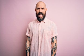 Poster - Handsome bald man with beard and tattoo wearing casual shirt over isolated pink background sticking tongue out happy with funny expression. Emotion concept.