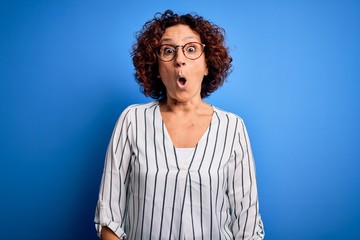 Poster - Middle age beautiful curly hair woman wearing casual striped shirt over isolated background afraid and shocked with surprise expression, fear and excited face.