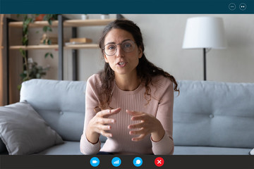 35s female teacher teach by video call explain educational material to trainee distantly seated on couch in living room at home. Friends communicating use videoconference app concept, pc screen view