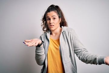 Sticker - Young beautiful sportswoman with curly hair wearing sportswear over white background clueless and confused expression with arms and hands raised. Doubt concept.