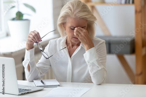 Cuadros en Lienzo Tired 60 years old businesswoman taking off glasses, suffering from dry eyes syndrome after long laptop use