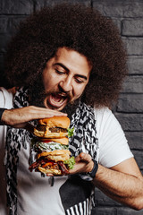 Curly guy open mouth to eat 3 burgers together. Healthy falafel burger, savory grilled chicken, and meaty angus beef burger. Emotional photo for promotion