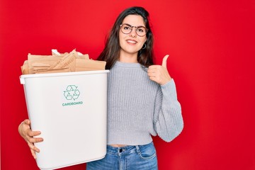 Sticker - Young beautiful woman holding recycle cardboard containter recycling for eco environment happy with big smile doing ok sign, thumb up with fingers, excellent sign