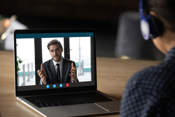 Woman wear headphones listen tutor during online class pc screen view over trainee shoulder. Colleague express opinion share ideas working together on project using video call, e-learn e-coach concept