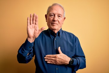 Wall Mural - Grey haired senior man wearing casual blue shirt standing over yellow background Swearing with hand on chest and open palm, making a loyalty promise oath