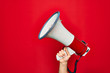 Beautiful hand of man holding megaphone over isolated red background