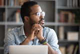 Fototapeta  - Pensive African American man in glasses distracted from computer work look in distance thinking or pondering, thoughtful biracial male lost in thoughts make plans visualizing, business vision concept