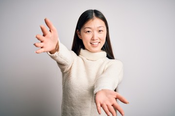 Sticker - Young beautiful asian woman wearing casual sweater standing over isolated background looking at the camera smiling with open arms for hug. Cheerful expression embracing happiness.