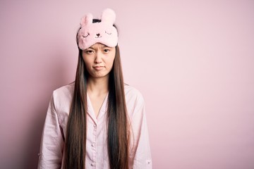 Sticker - Young asian woman wearing pajama and sleep mask over pink isolated background skeptic and nervous, frowning upset because of problem. Negative person.