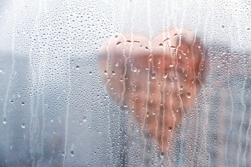 Heart shape painted on glass wet window with drops of rain in city