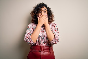 Poster - Young beautiful curly arab woman wearing floral t-shirt standing over isolated white background shocked covering mouth with hands for mistake. Secret concept.