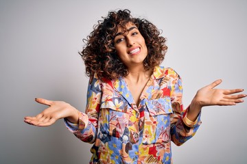 Poster - Young beautiful curly arab woman wearing floral colorful shirt standing over white background clueless and confused expression with arms and hands raised. Doubt concept.