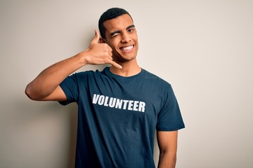 Young handsome african american man volunteering wearing t-shirt with volunteer message smiling doing phone gesture with hand and fingers like talking on the telephone. Communicating concepts.