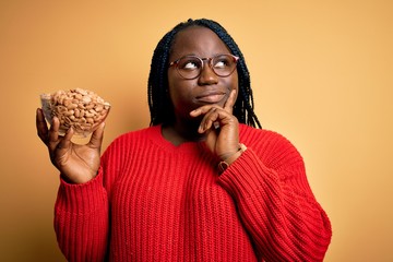 Sticker - Young african american plus size woman with braids holding bowl with healthy peanuts serious face thinking about question, very confused idea