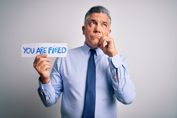 Poster - Middle age grey-haired man fired with problems holding paper with you are fired message serious face thinking about question, very confused idea