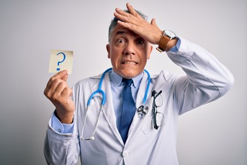 Poster - Middle age handsome grey-haired doctor man holding paper with question mark stressed with hand on head, shocked with shame and surprise face, angry and frustrated. Fear and upset for mistake.