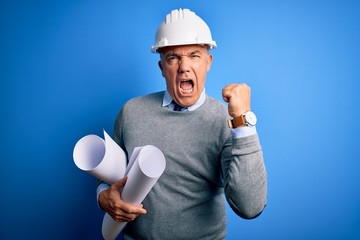 Poster - Middle age handsome grey-haired architect man wearing safety helmet holding blueprints angry and mad raising fist frustrated and furious while shouting with anger. Rage and aggressive concept.