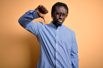 Poster - Young handsome african american man wearing shirt and glasses over yellow background looking unhappy and angry showing rejection and negative with thumbs down gesture. Bad expression.