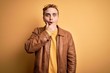 © Krakenimages.com - Young handsome redhead man wearing casual leather jacket over isolated yellow background Looking fascinated with disbelief, surprise and amazed expression with hands on chin
