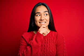 Poster - Young beautiful asian woman wearing casual sweater standing over isolated red background with hand on chin thinking about question, pensive expression. Smiling with thoughtful face. Doubt concept.