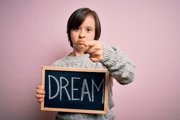 Sticker - Young down syndrome woman holding blackboard with dream word as message of happiness pointing with finger to the camera and to you, hand sign, positive and confident gesture from the front