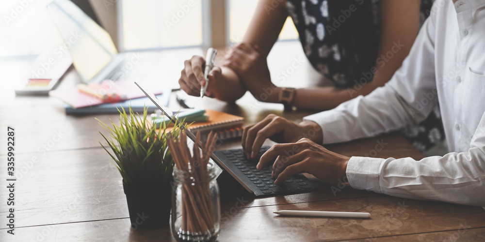 Cropped image of marketing team holding a stylus pen and typing on computer tablet with keyboard case while sitting and working together at the wooden working desk. Collaboration concept. - obrazy, fototapety, plakaty 