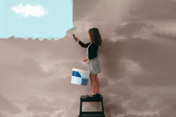 little girl uses a can of paint to color the wall of the room from cloudy gray to clear blue sky - p