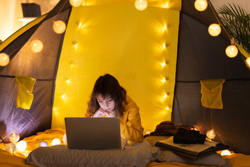 Wall Mural - little 11 year old girl using laptop under her home-made tent inside the living room.