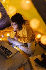 Wall Mural - little 11 year old girl using laptop under her home-made tent inside the living room.