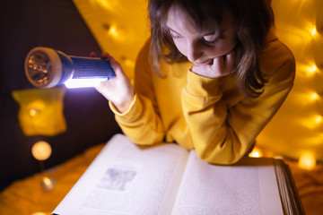 Wall Mural - young female child reading encyclopedia in a home made livingroom tent with light balls.