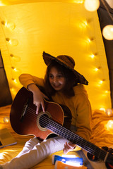 Wall Mural - little girl playing acoustic guitar under the tent in a living room.