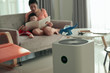 © sutichak - air purifier in living room with mother and kid reading inside home