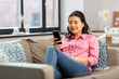 © Syda Productions - people, technology and leisure concept - happy smiling asian young woman in pink shirt with smartphone sitting on sofa at home