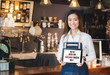 © weedezign - asian barista holding tabblet sign we’re open for takeaway orders only infront of counterbar.social distancing concept when coronavirus is outbreak in city
