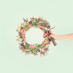 Wall Mural - Female women hand holding summer flowers wreath with ribbon at light mint background. Creative flowers arrangement concept