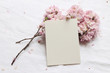 © tabitazn - Wedding spring styled stock photo. Feminine desktop mockup scene with pink blossoming Japanese cherry tree branches and blank paper greeting card on white linen table background. Flat lay, top view.