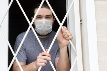 male model in a disposable mask, dark hair, beard and grey t-shirt.A coronavirus patient remains at home under quarantine and disease prevention.Sad and negative Emotions in the eyes of a person