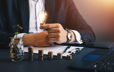 Hand businessman holding a light bulb with coins stack. Successful businessman. Creative ideas for saving money concept. Concept inspiration and innovation.