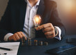 © Miha Creative - Hand businessman holding a light bulb with coins stack. Successful businessman. Creative ideas for saving money concept. Concept inspiration and innovation.