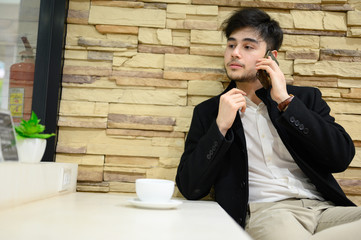 Portrait smiling and happy man playing mobile phone.Handsome business young man sitting on chair and drinking coffee in the restaurant.