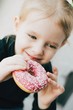 little beauty  blonde smiling girl eating pink donut.