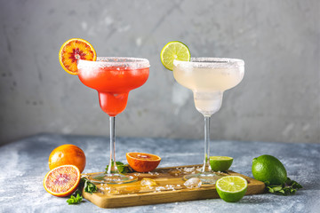 Frozen lime margarita and blood orange margarita cocktail mix in salt rimmed glasses garnished with slices of lime and orange. Focus on the citrus slice