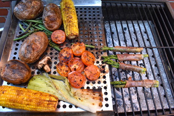 Summer side dishes cooked on the barbecue Corn on the cob mushrooms green beans leeks tomatoes whole red potatoes asparagus wrapped in prosciutto ham Vegetables and meaty starter on the outdoor grill