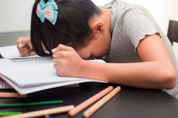 Frustrated student girl at home, she is resting with her face down on the school book with an angry gesture with his arms. Concept of education and childhood.