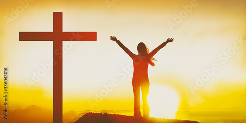 Easter Christian cross woman praising the Lord with hands raised in sunset flare glow outside. Sunday worship service