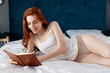© Dmitrii Kotin - Redhead woman lying and relax on the bed and looks in her diary.